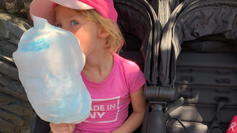 A young girl sitting in a stroller eating a large puff of cotton candy