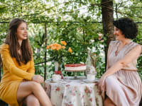 Two women smiling while enjoying tea in a garden.