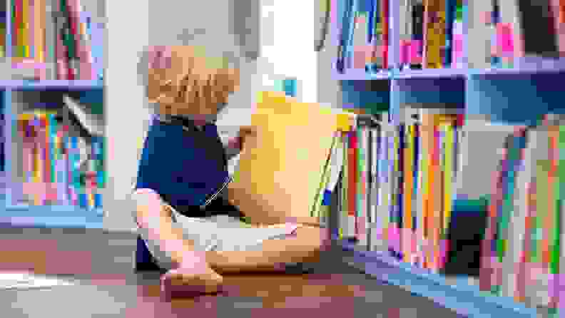 A small child pulling books off a bookshelf