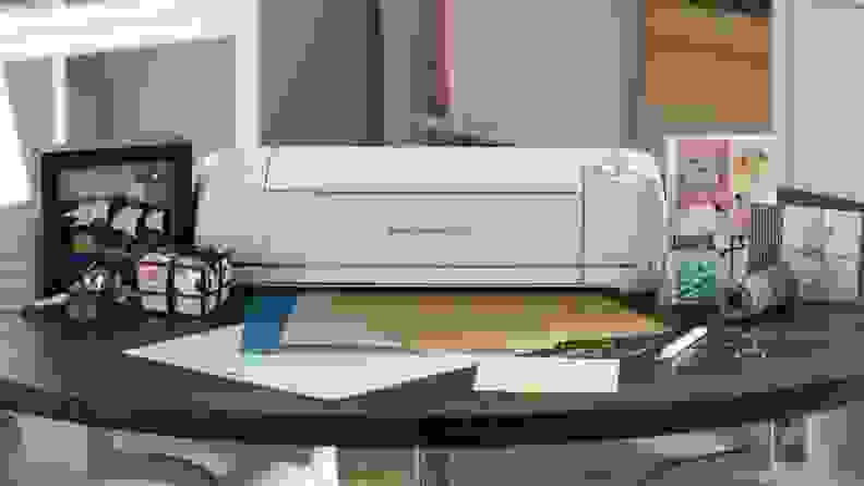 A Cricut machine sitting on a table surrounded by craft paper.