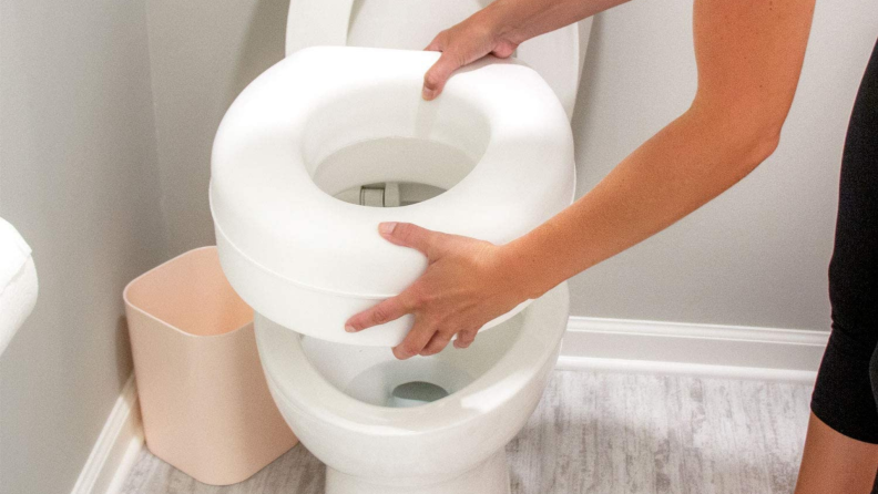 A person installs an elevated toilet seat.