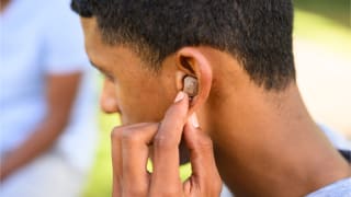 A person pushes a hearing aid into their ear in an outside setting