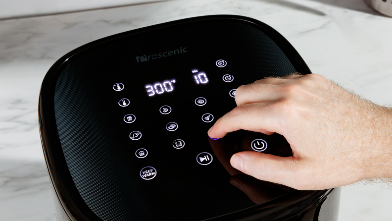 Person using fingers to press keypad buttons of the Proscenic T22 Air Fryer.