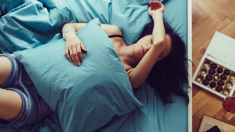 a person lies on her back in bed with chocolate and her phone