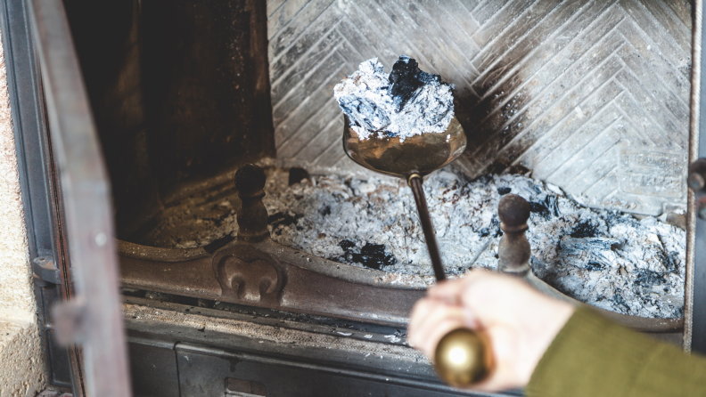 Person using shovel to remove ash from fireplace.