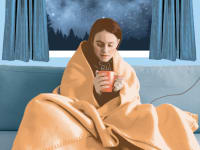 woman sitting on the couch in front of the window drinking tea wrapped in electric blanket