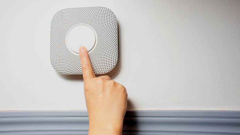 A person testing a dual carbon monoxide and fire detector.