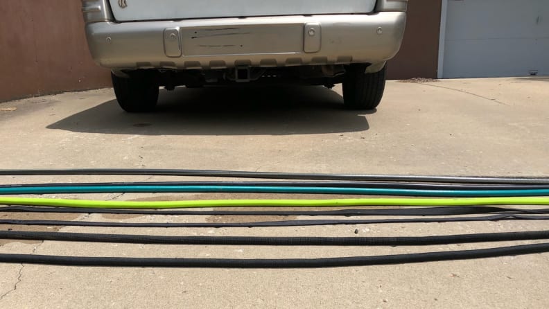 Eight garden hoses stretch across a driveway near a car.