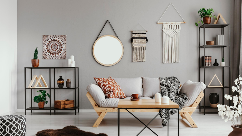 A wall with two macrame hangings, a round mirror, and an art print