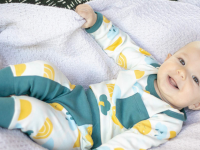 Baby smiling on blanket while wearing green and yellow clothing set.