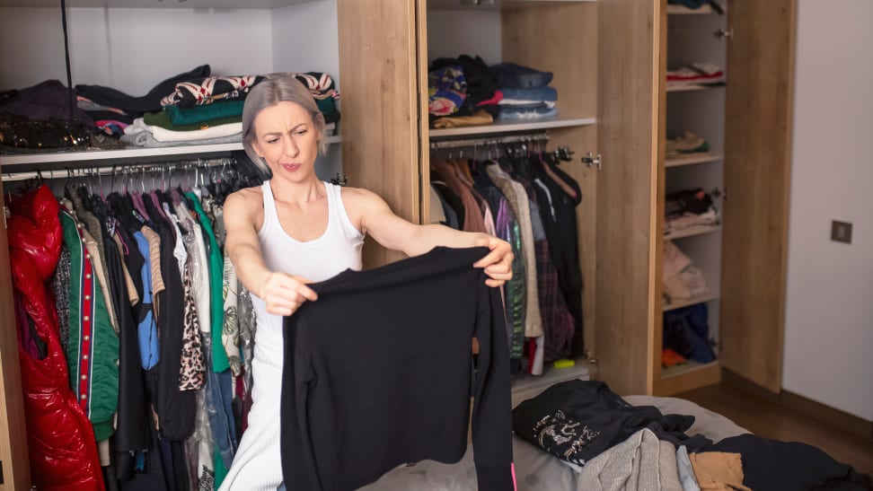 Woman inspecting black sweater in her closet.