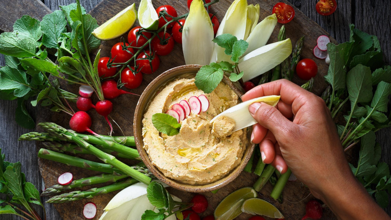 Person dipping vegetable in hummus
