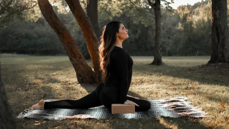 A yogi, dressed in all black, holds a pose on a blanket outdoors.