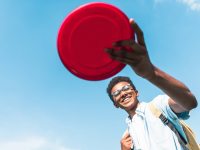 A child flings a red frisbee outside.