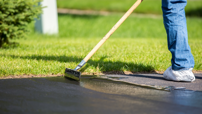 Person using squeegee to spread sealer onto driveway.