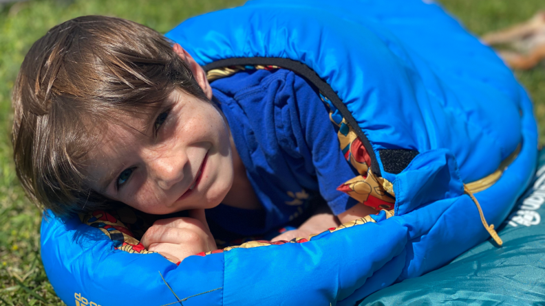 A child smiles in an REI Kindercone sleeping bag