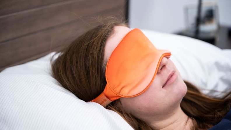Person laying mattress with orange satin sleep mask.