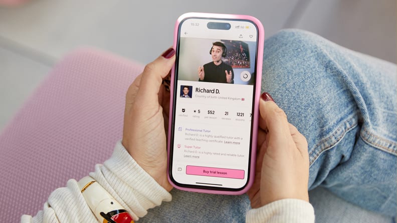 A person uses a smartphone to browse an online learning platform showing a tutor profile with video, ratings, and lesson pricing.