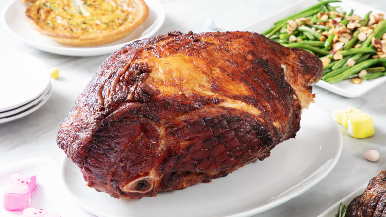 A whole bone-in ham sits on a serving platter surrounded by other side dishes.