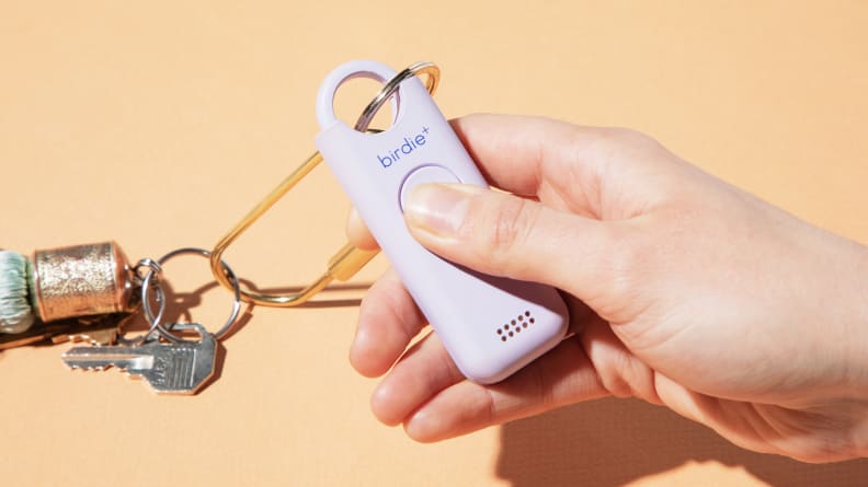 A person holding the She's Birdie+ with a keychain attached to it, on an orange background.