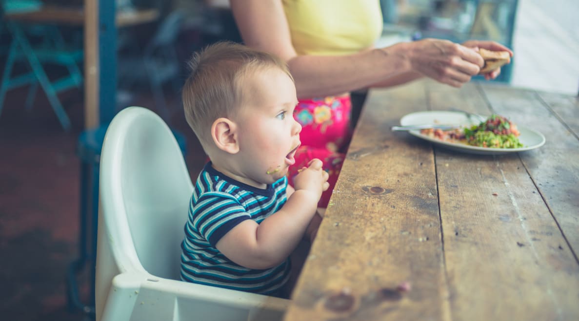 A toddler sits on a booster seat at the dinner table.