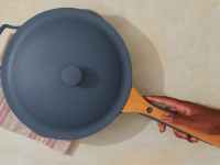 A person grabs the handle of a blue ceramic pan.
