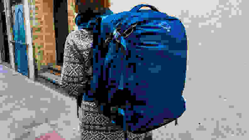 A person wearing a fully loaded Osprey travel backpack.