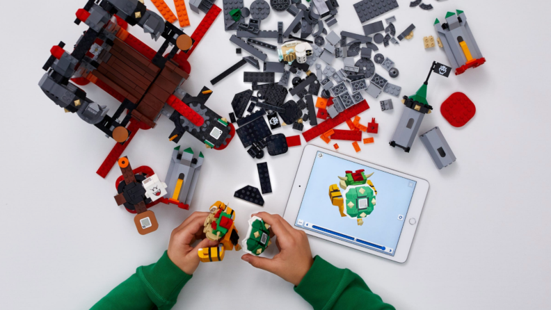 A child's hands build a Lego set over an app shown on an iPad.