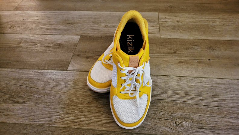 Top-down view of bright yellow and white Kizik Brisbane sneakers on woodgrain flooring