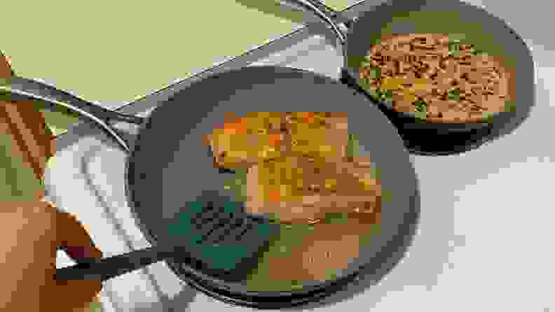 A person uses a spatula to flip salmon fillets in a nonstick skillet.