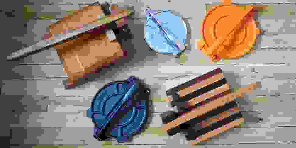 Five tortilla presses laid out on a wooden background, shot from above.