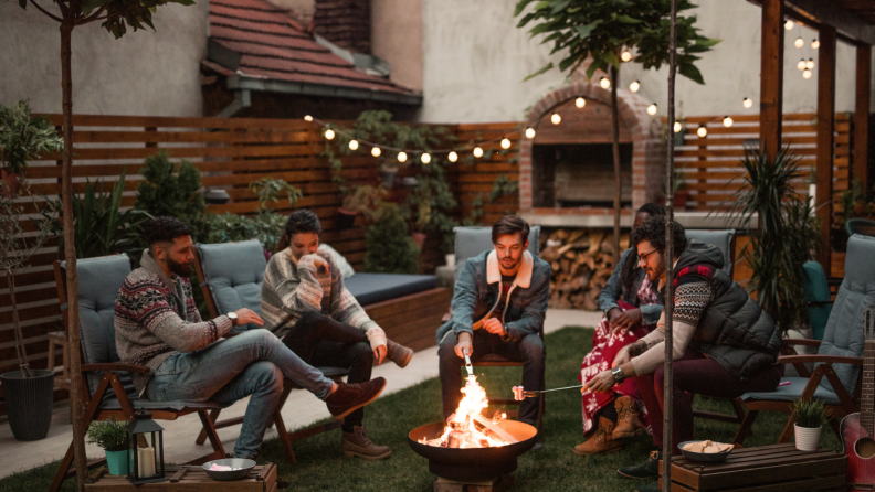 Group of friends gathered in outdoor space around open fire.