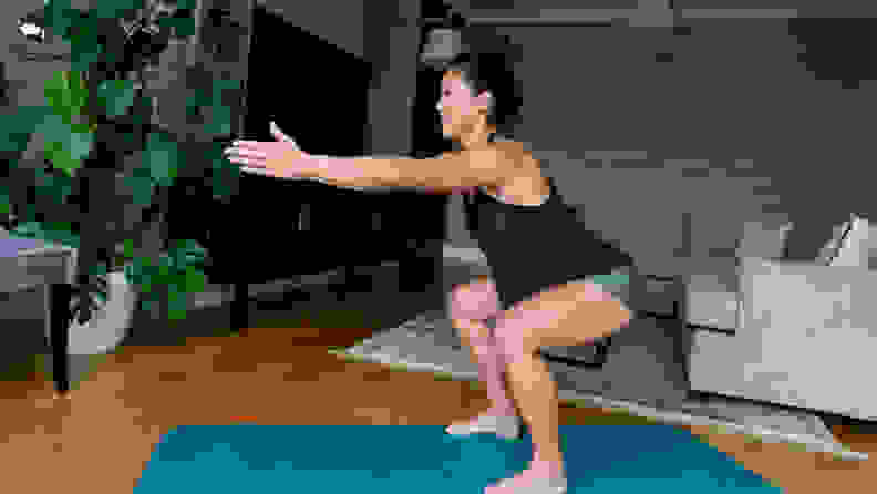Active pregnant woman holds a squat position while exercising in her home.