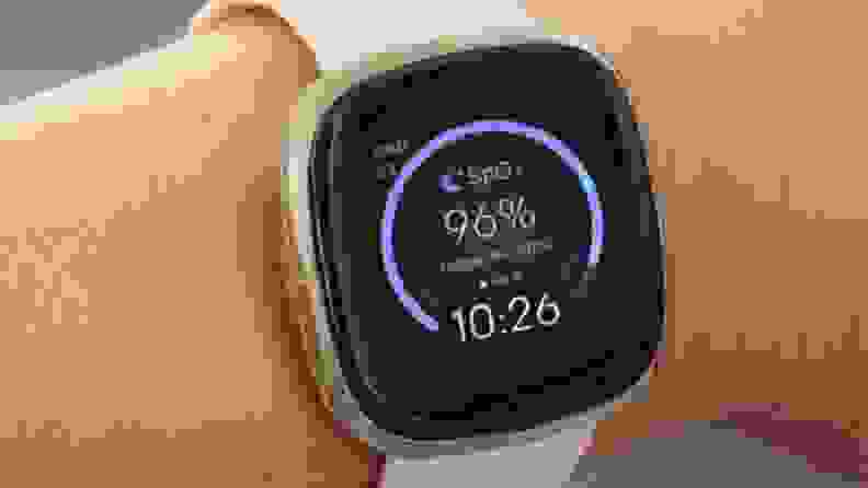 a woman's wrist showing the fitbit sense with a clock face illuminated
