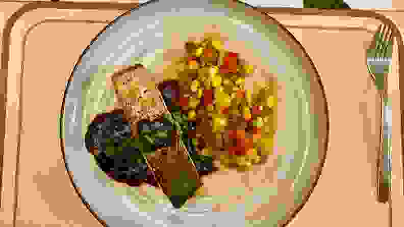 A plate of grilled salmon, succotash, and parsley sauce sits on a placemat.
