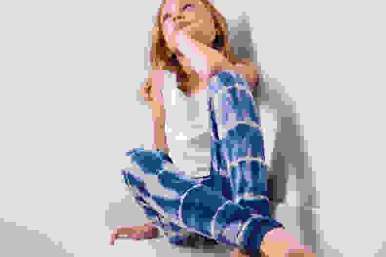 A girl wearing a pair of blue tie dye pants sits cross legged