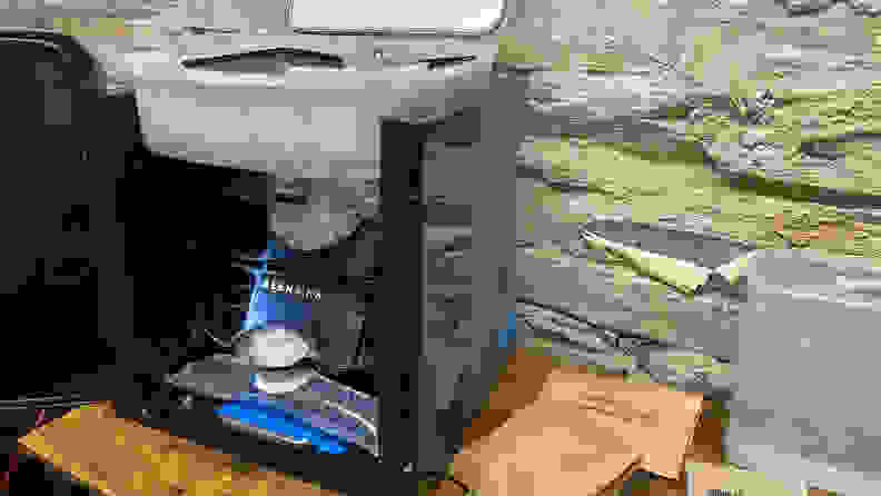 A Beermkr machine with its front door open is on top of a table. Some brown bags are scatted around the machine.