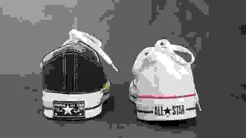 On the left, a Chuck 70 low top sneaker in black. On the right, a white Chuck Taylor All Star low top sneaker. Both sneakers feature different logos on their heels.