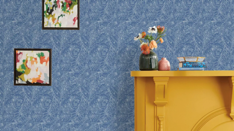 A light blue wallpaper is pasted on the walls. Hanging on the wall are two picture frames. There is a mustard yellow fireplace on the right side of the photo.