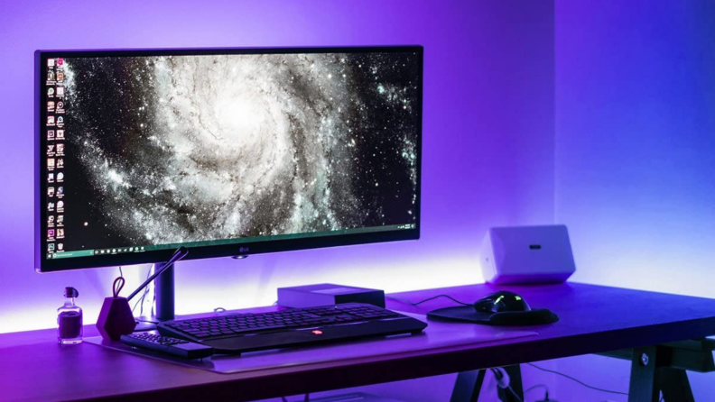 Desk with desktop monitor and keyboard surrounded by a purple LED light glow