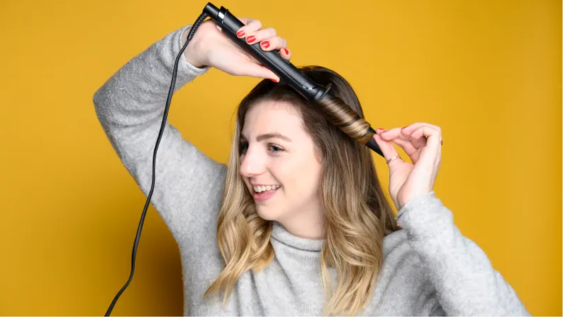 An image of a woman using a curling wand on her hair.
