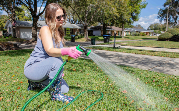 A person watering the grass with a garden hose