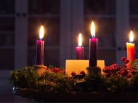 Lit advent wreath with four candles on an evergreen wreath and a white pillar candle in the center.