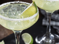 Margarita glasses filled with margarita, and lime wedges, rimmed with salt