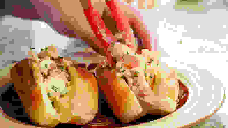 A person is using a pair of tongs to stuff the sandwich buns with lobster salad.