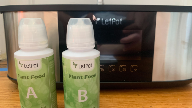 Two bottles of LetPot plant food stand in front of the LetPot hydroponic garden.