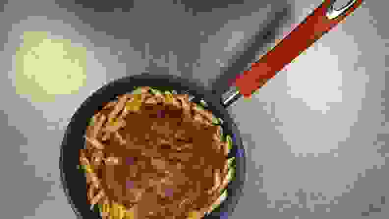 A nonstick frying pan filled with pasta that's covered in sauce and shredded parmesan.