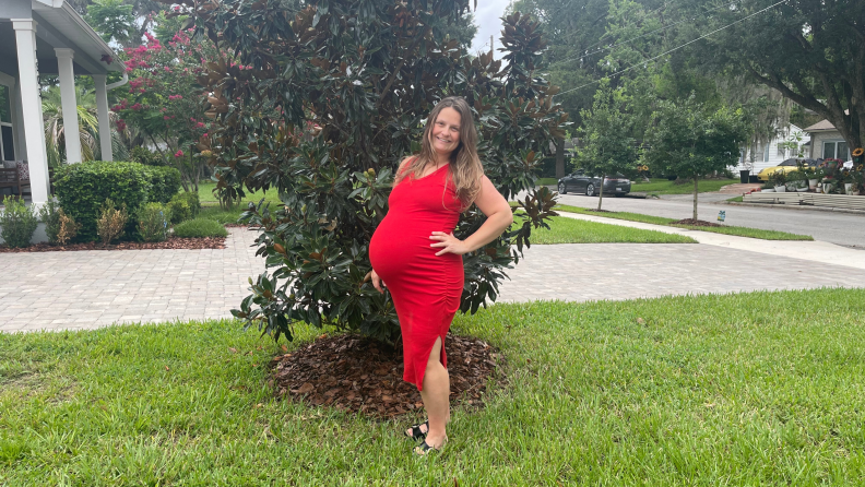 Writer, Rachel Murphy, wearing a red long dress and the Skims Maternity Sculpting Bodysuit Mid-thigh, while standing outside.