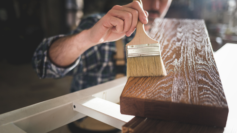 A person applies a topcoat of varnish on a wooden board.