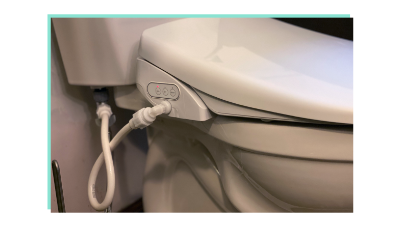 Close-up shot of the side of a toilet showing the bidet hooked up.